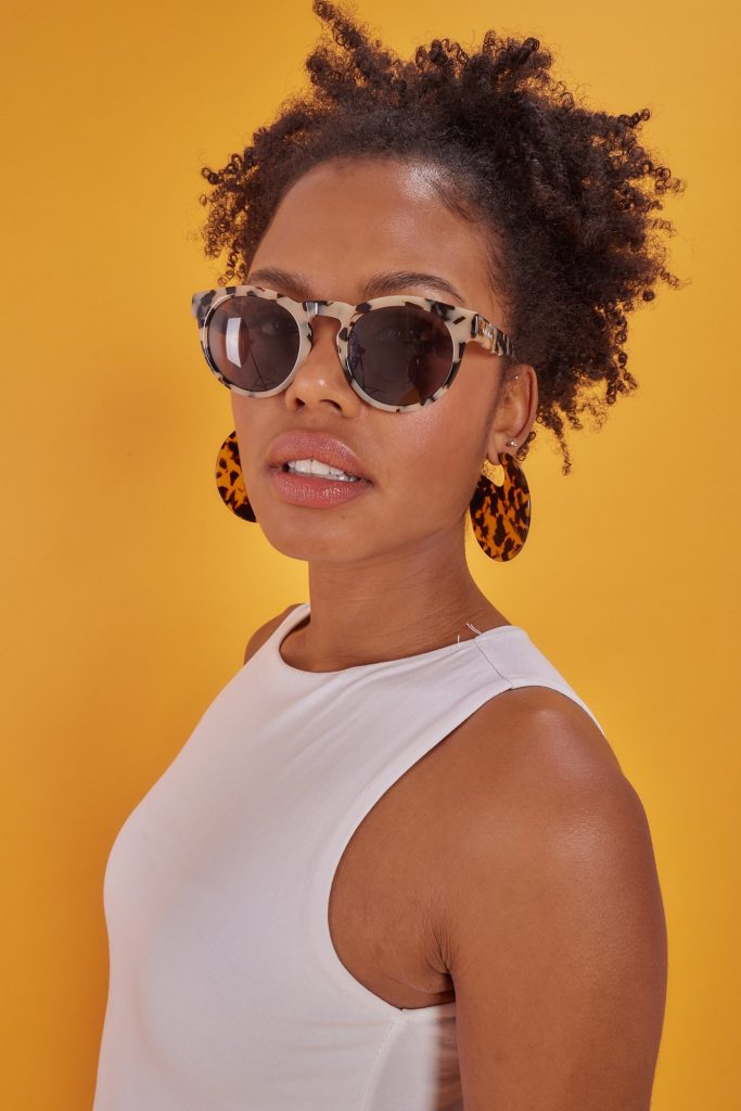 Frau mit Sonnenbrille und weißem Top vor gelbem Hintergrund