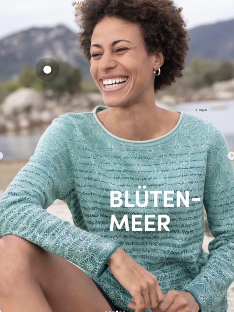 Katalogseite „Blütenmeer“: lachende Frau im türkisen Strickpullover am Strand