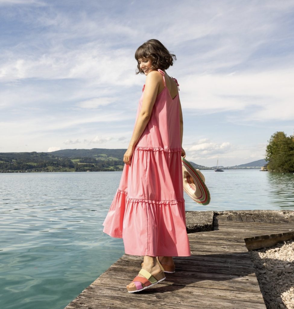 Frau im rosa Stufenkleid auf einem Steg am See