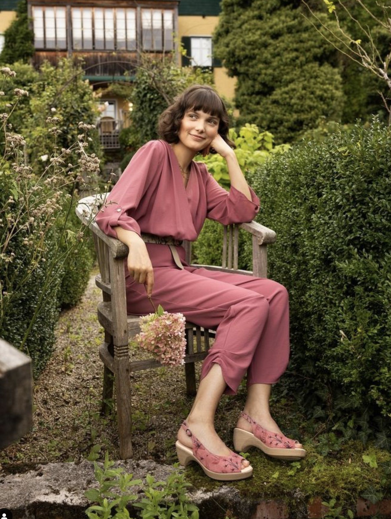 Frau im rosa Overall sitzt auf einem Gartenstuhl