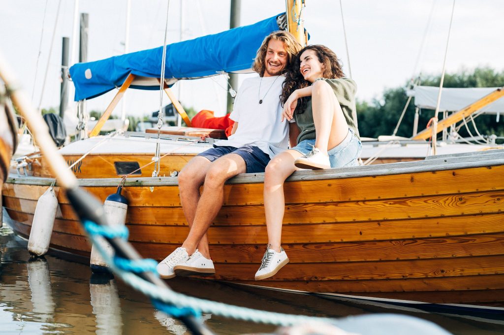 Paar sitzt lachend auf einem Holzboot im Hafen