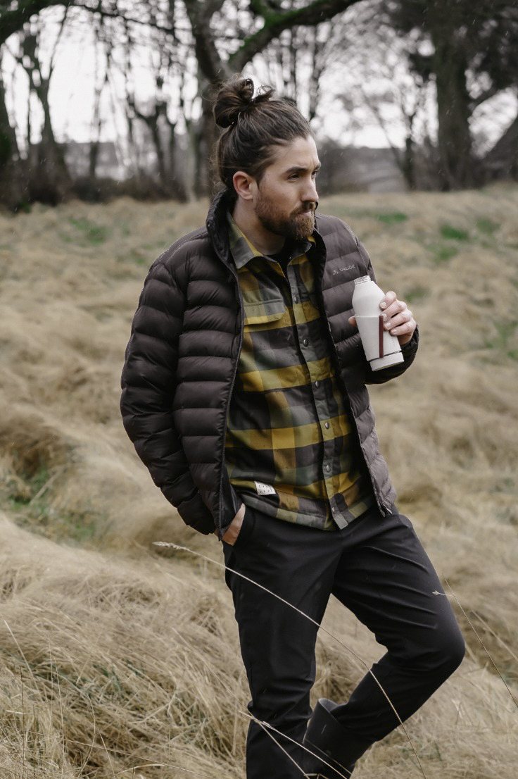 Mann in Steppjacke und kariertem Hemd mit Trinkflasche im hohen Gras